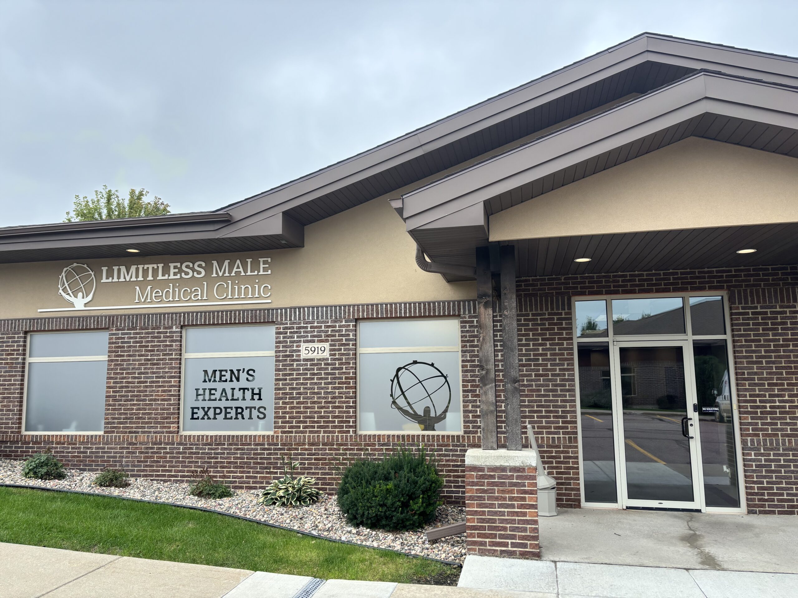 Front view of the Limitless Male Medical Clinic with a brick exterior, glass windows, and the 'MEN'S HEALTH EXPERTS' sign visible in the windows.