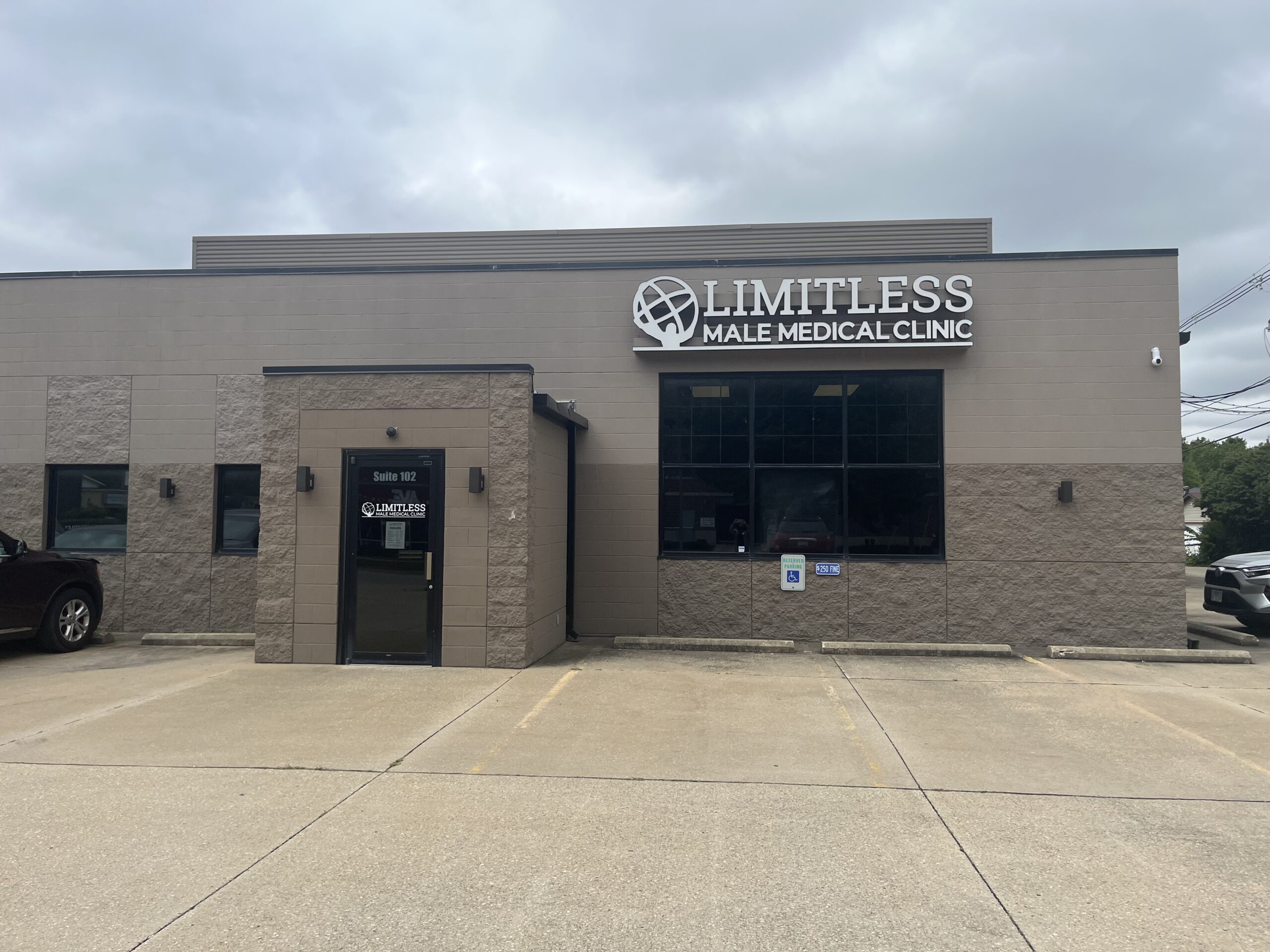 Front view of a beige clinic building with a large 'LIMITLESS MALE MEDICAL CLINIC' sign above the entrance. Grey cloudy sky in background.
